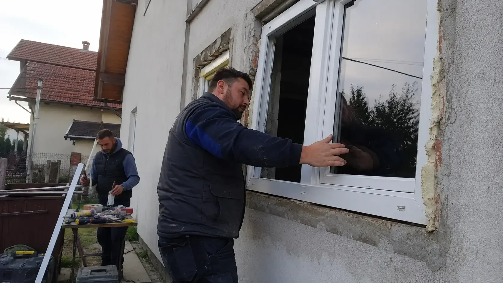 Profesionalni monter ugrađuje Rehau PVC prozor u fasadu domaćinstva, alati vidljivi na licu mesta.