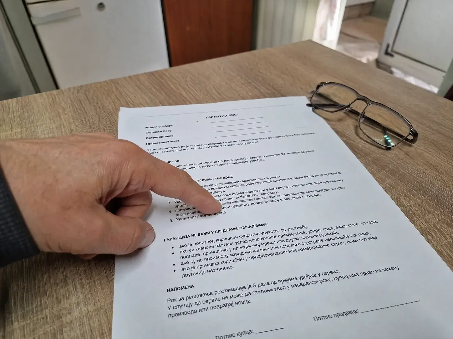 Garancijski list na stolu, ruka pokazuje na jednu od stavki, naočare za čitanje pored.