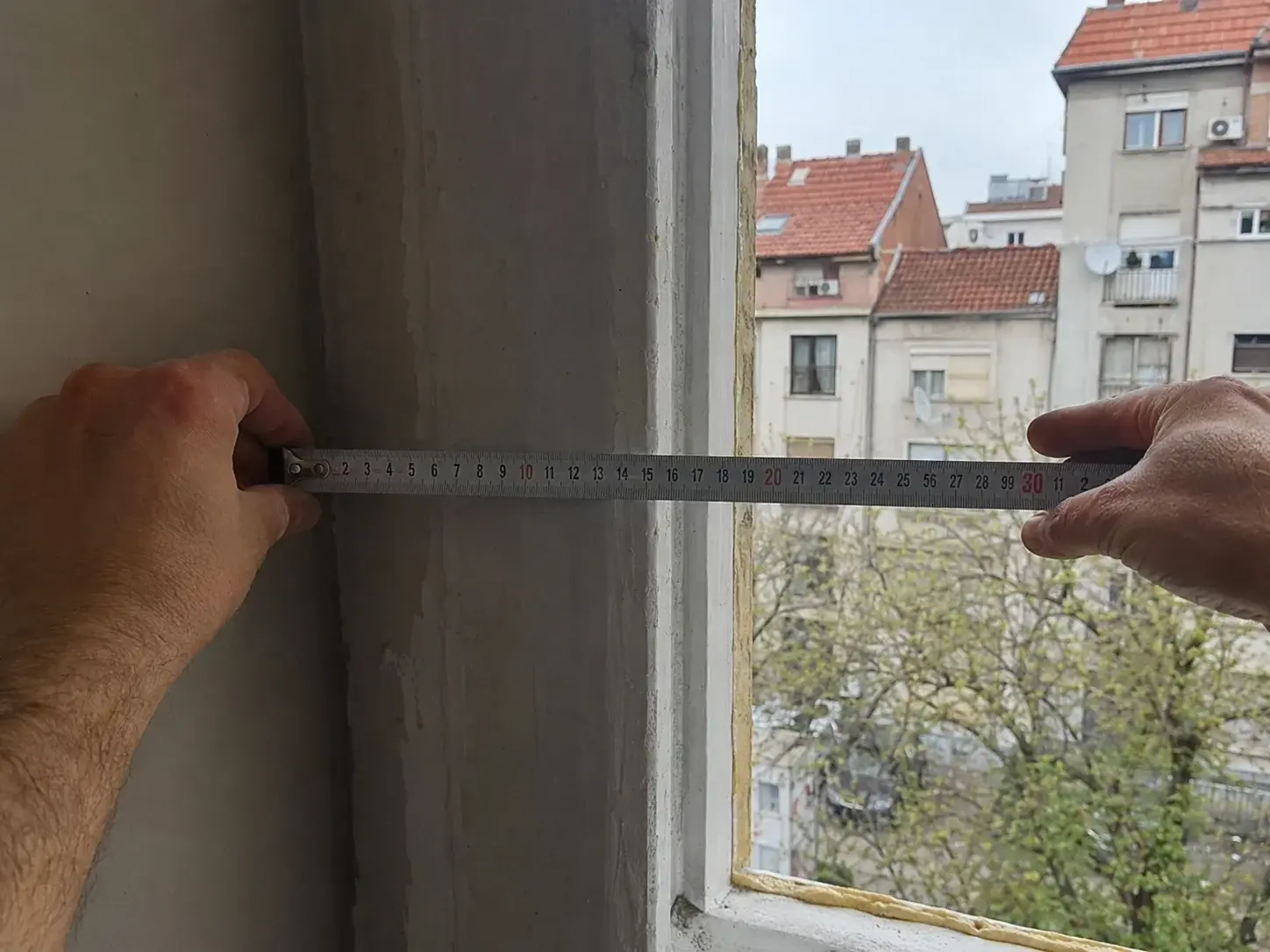 Ruke mere širinu otvora prozora čeličnim metrom razvučenim preko, vidljive cifre.