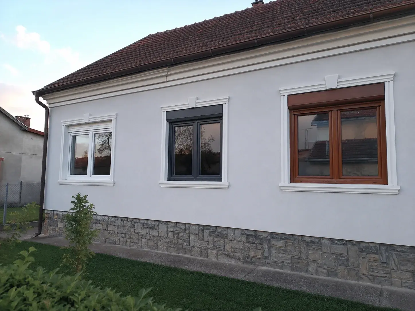 Fasada kuće sa tri različita PVC prozora: beli, antracit i u boji drveta, jedan do drugog.