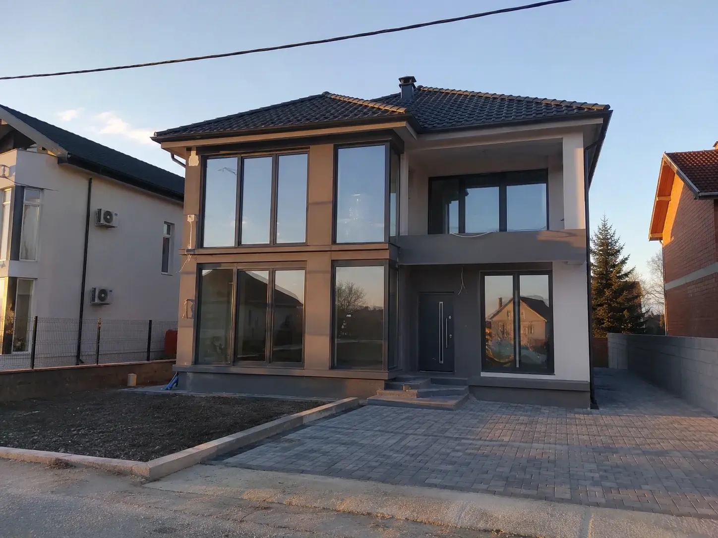 Moderna kuća sa velikim prozorima od poda do plafona, antracit PVC ramovi, popodnevno sunce.