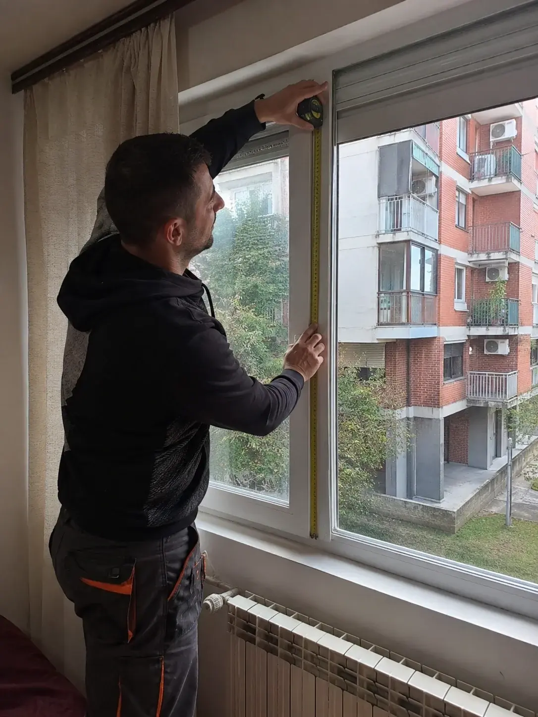 Vlasnik stana meri visinu prozora metrom iznutra, fokus na precizno merenje.