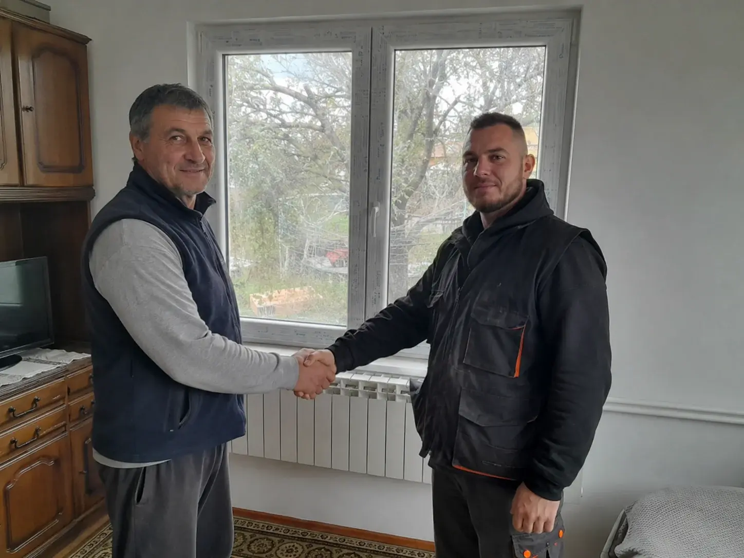 Vlasnik kuće i monter se rukuju pored novog PVC prozora sa zaštitnom folijom.