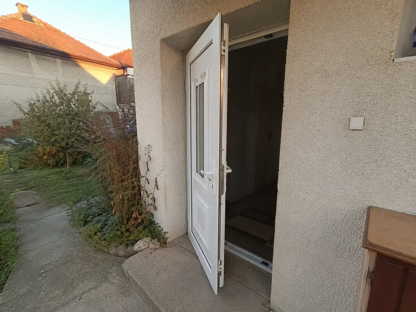 Nova bela PVC ulazna vrata na fasadi kuće, blago odškrinuta sa vidljivim mehanizmom zaključavanja.
